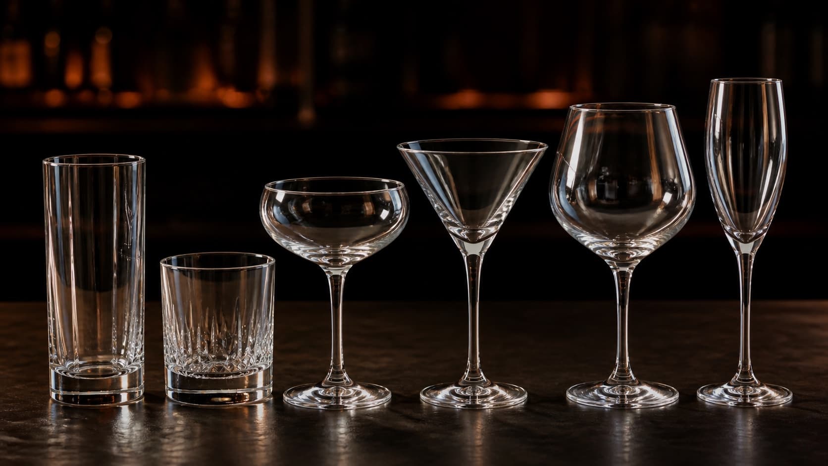 Tomma highballglas, old fashioned-glas, coupeglas, martiniglas, vinglas och champagneglas på en mörk bardisk.