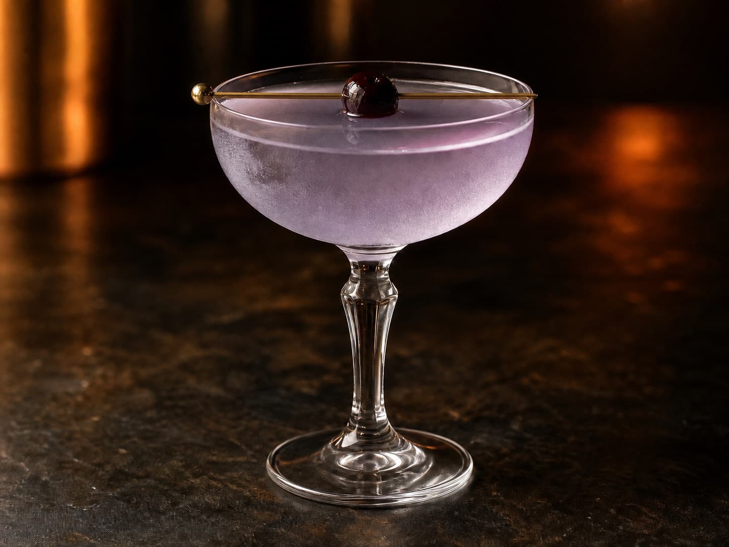 Aviation i ett kylt coupeglas med ljuslila cocktail och ett cocktailkörsbär.
