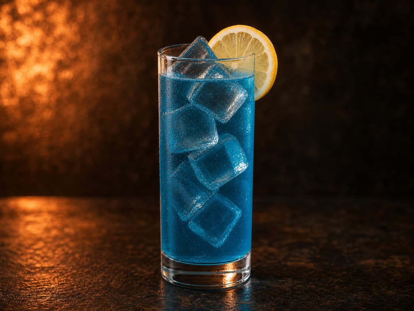 Blue Lagoon i ett högt glas med is, klar turkosblå dryck och citronskiva.