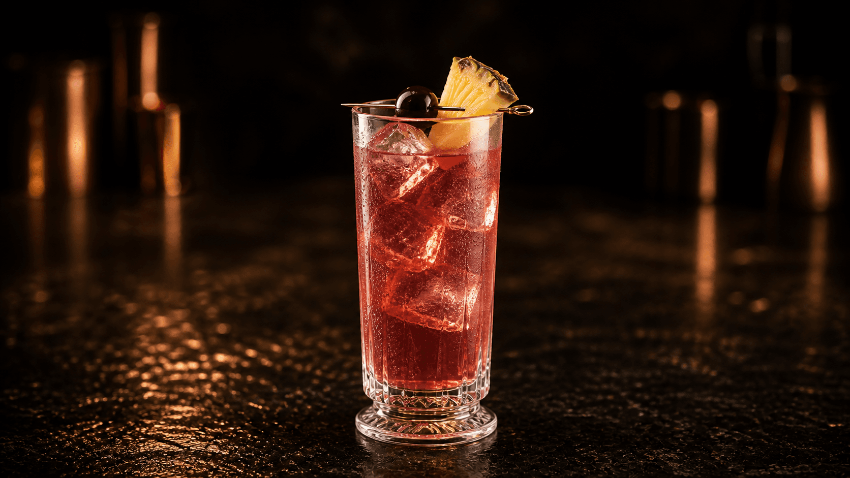 Singapore Sling i ett högt glas med rosa-röd cocktail, is, ananas och cocktailkörsbär.