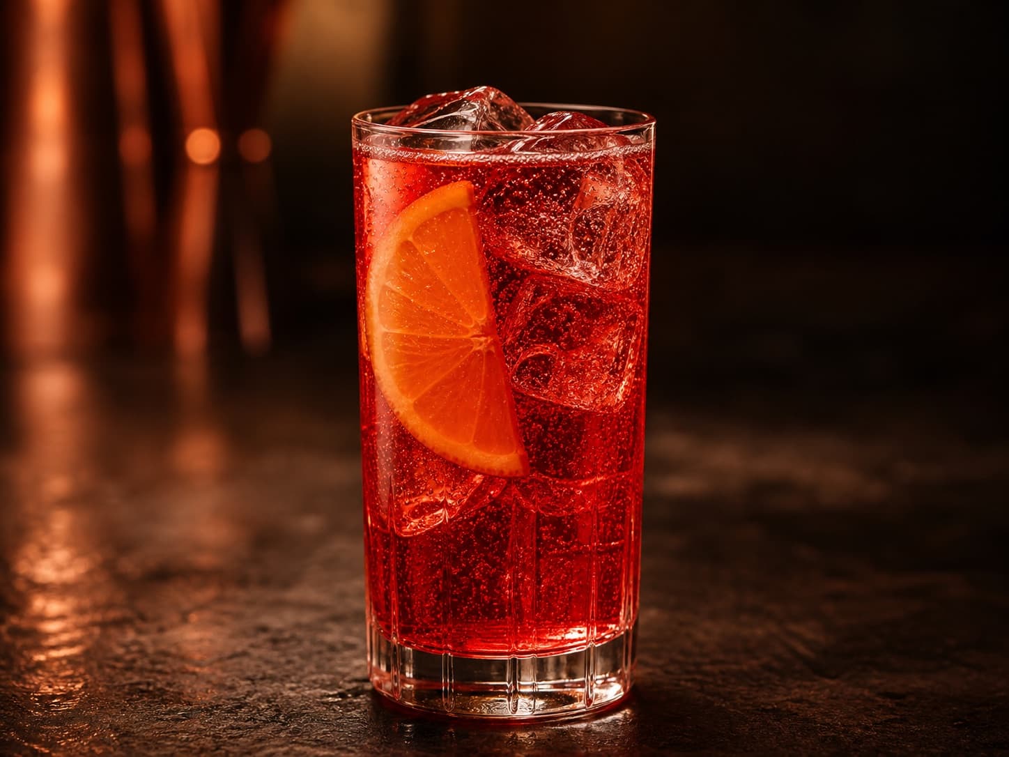 Campari Soda i ett highballglas med klar rubinröd drink, is och en apelsinskiva.