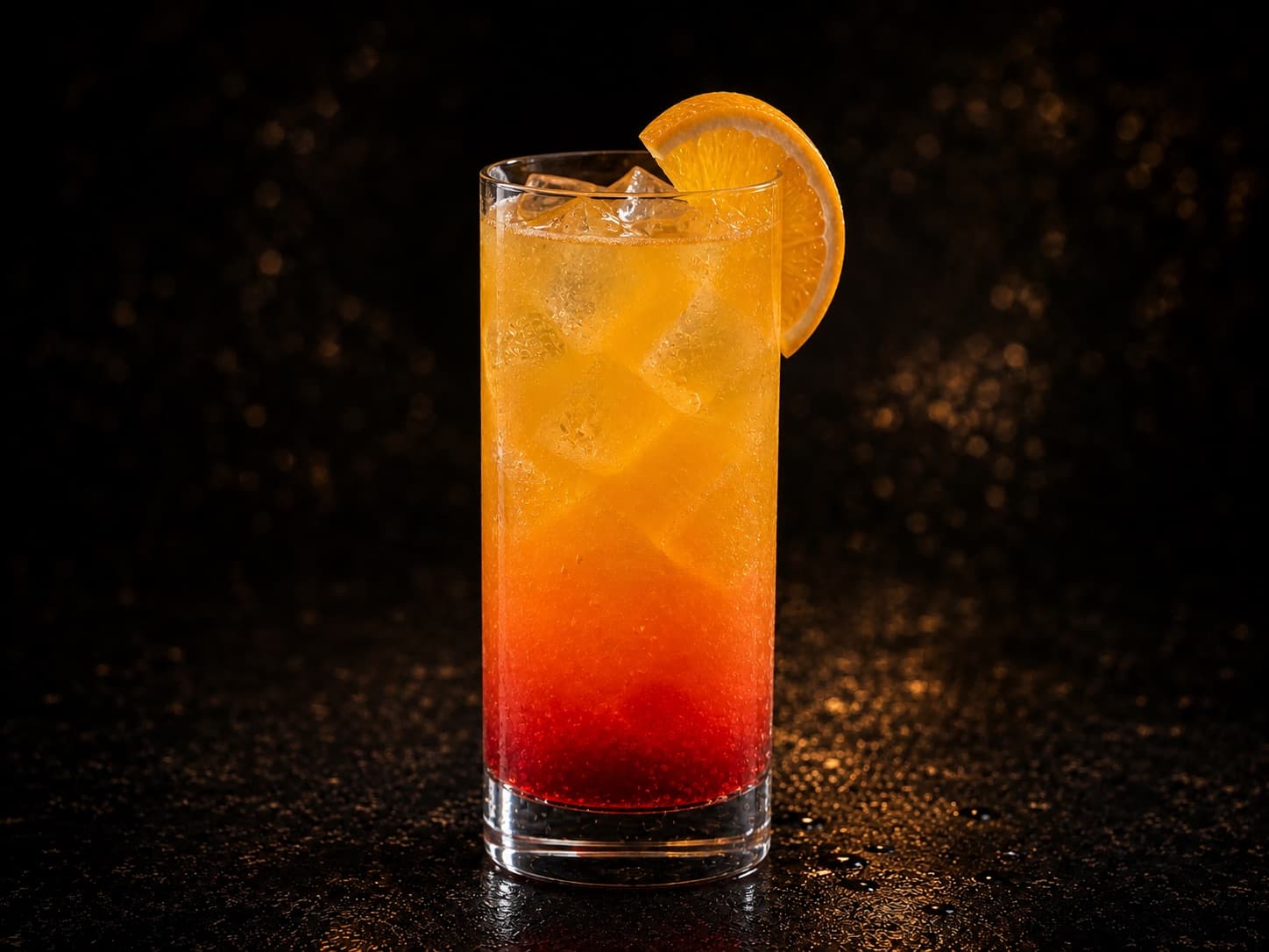 Virgin Tequila Sunrise i ett highballglas med orange drink, röd grenadinbotten och is.